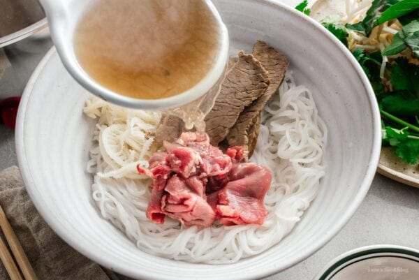 ladling pho soup over steak | foodiesanddrink.com